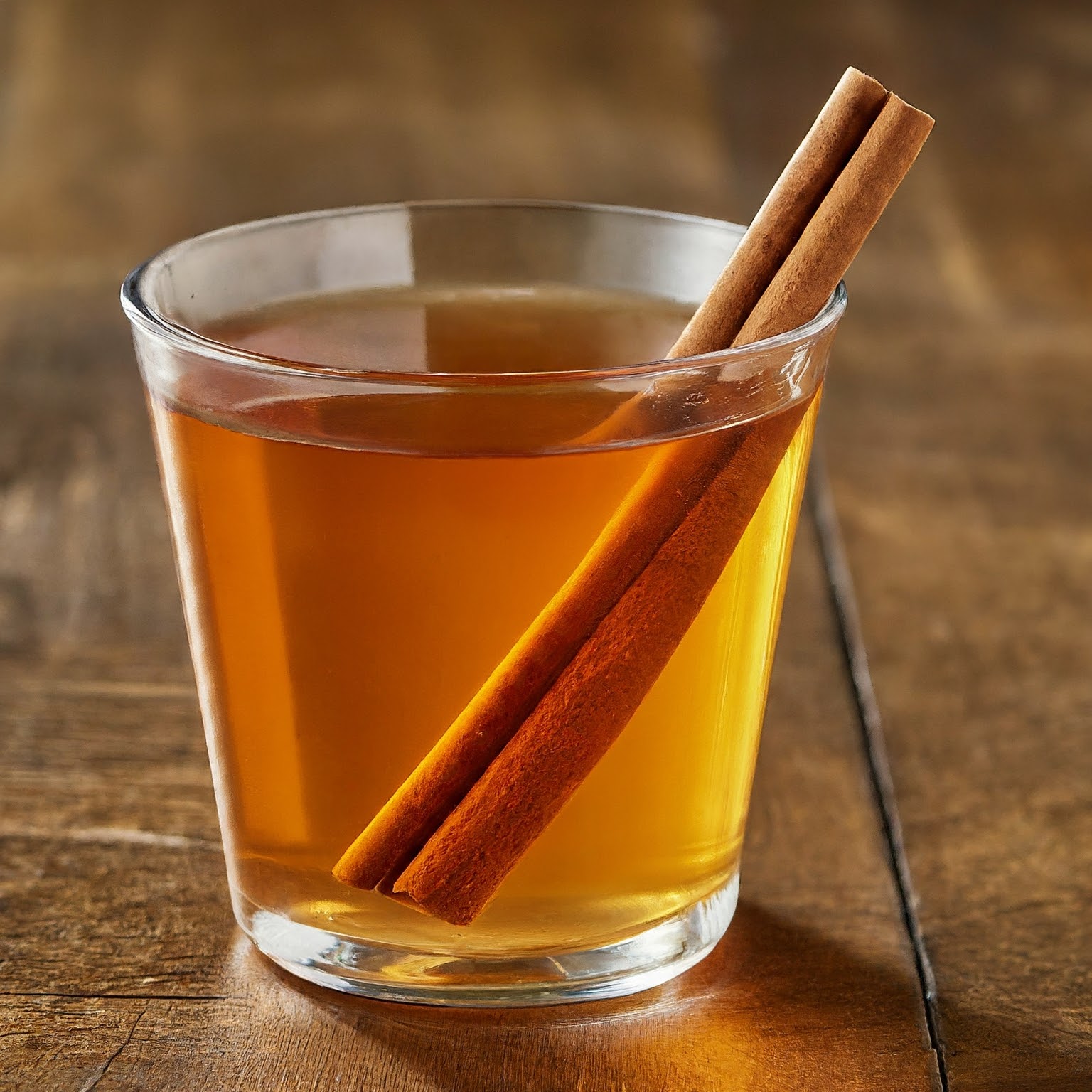 A glass of apple pie moonshine and a cinnamon stick on a wooden table